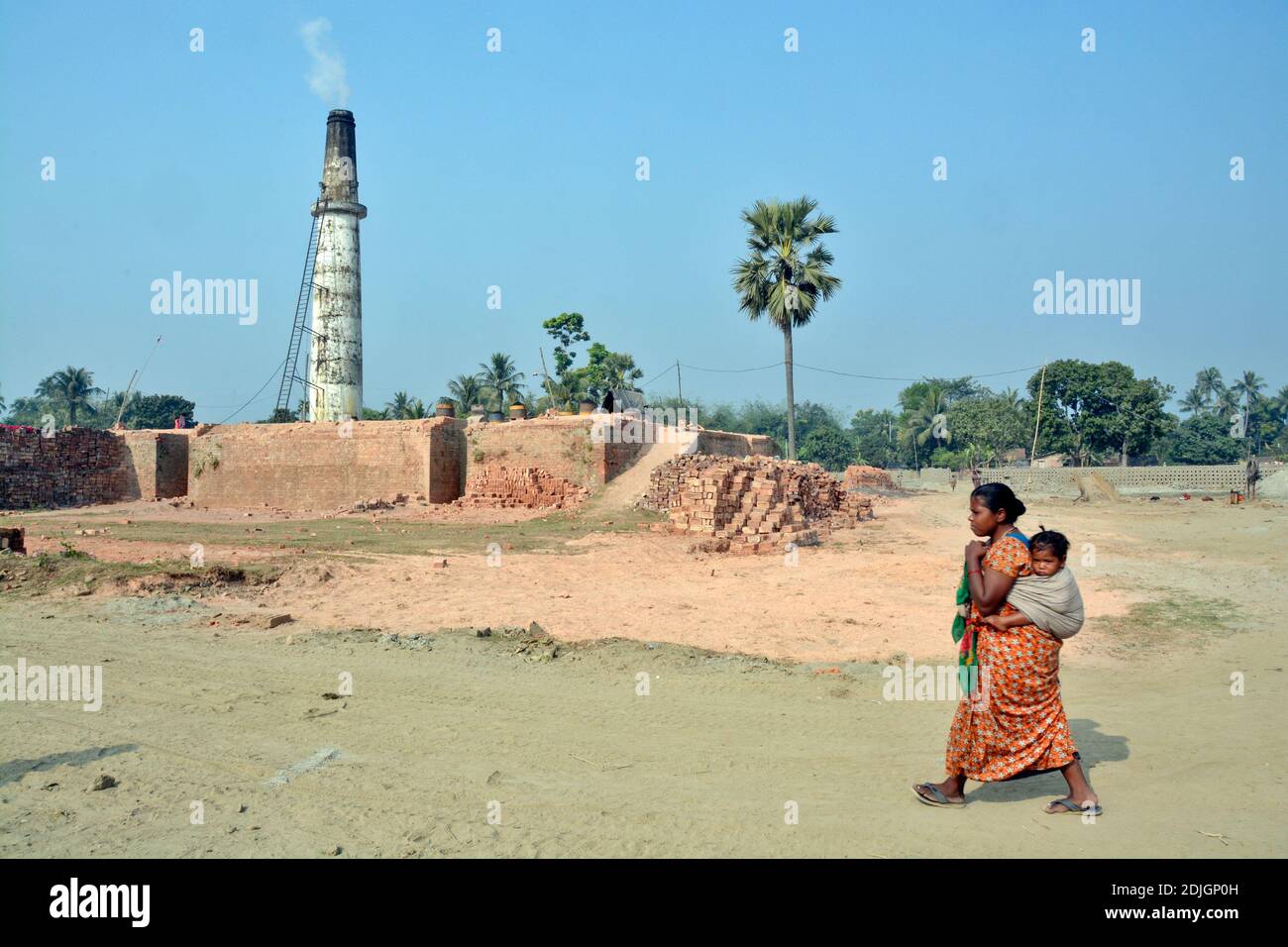 Picture of a brick kiln in rural West Bengal.The mother wraps the baby in a towel on her back and returns to her home after work. Stock Photo