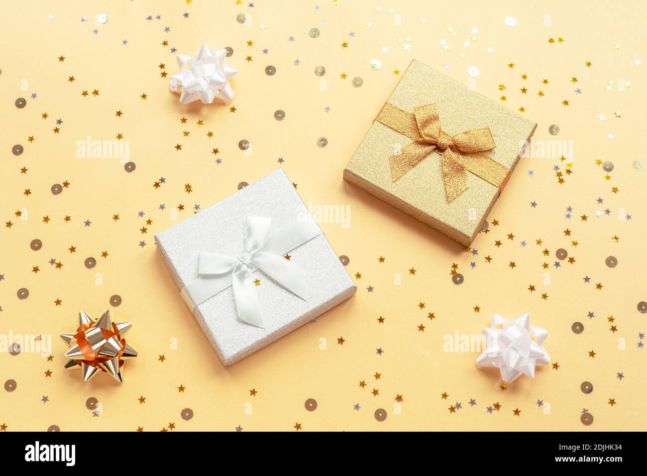 Two gifts in boxes on yellow backgound with baubles and confetti. Christmas, New Year concept. Top view, flat lay. Stock Photo