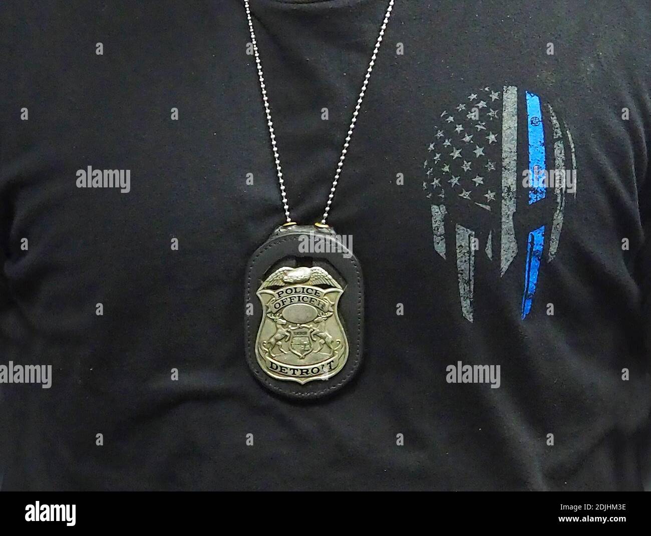 Detroit police badge hangs around an officers neck on a chain, over an American flag and Thin Blue Line motif t-shirt Stock Photo