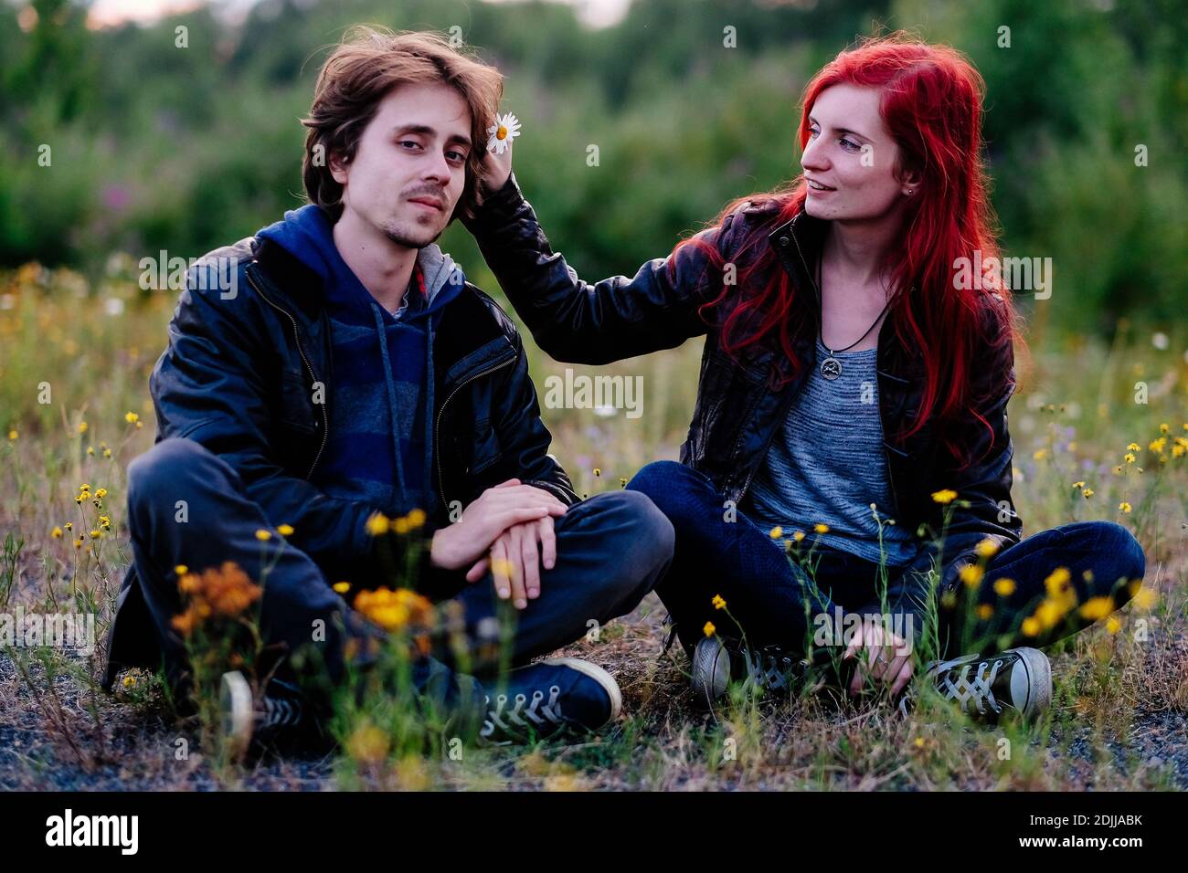 Redhead Girlfriend Putting Flower In Boyfriend Hair While Sitting On Field  Stock Photo - Alamy