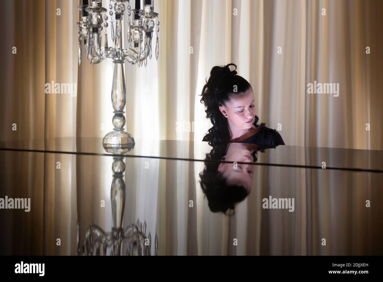 Elegant woman Pianist playing grand piano with reflection on the black piano surface Stock Photo