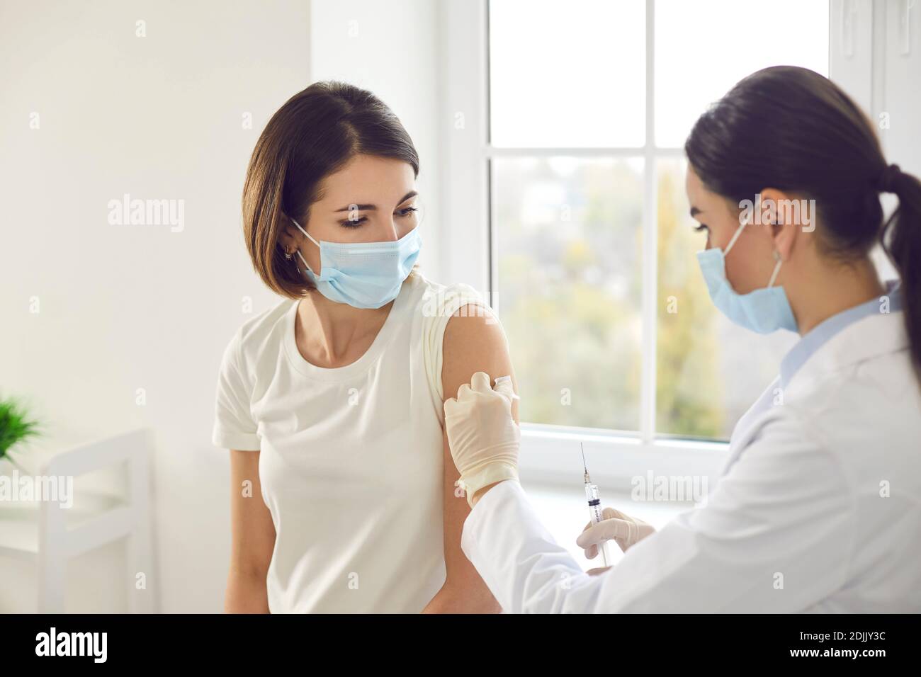 Young woman in a protective face mask getting an antiviral vaccine at the clinic Stock Photo