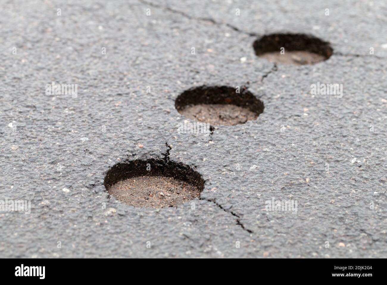 Damaged asphalt road with cracks and pavement test holes, close-up photo Stock Photo