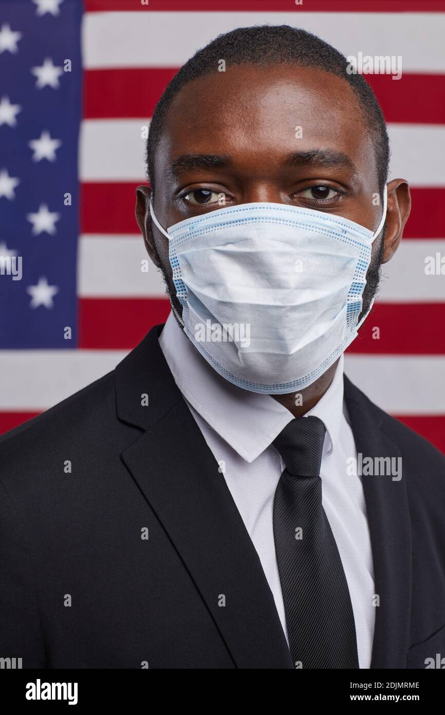 Vertical portrait of African-American politician wearing mask and looking at camera while standing against USA flag background Stock Photo