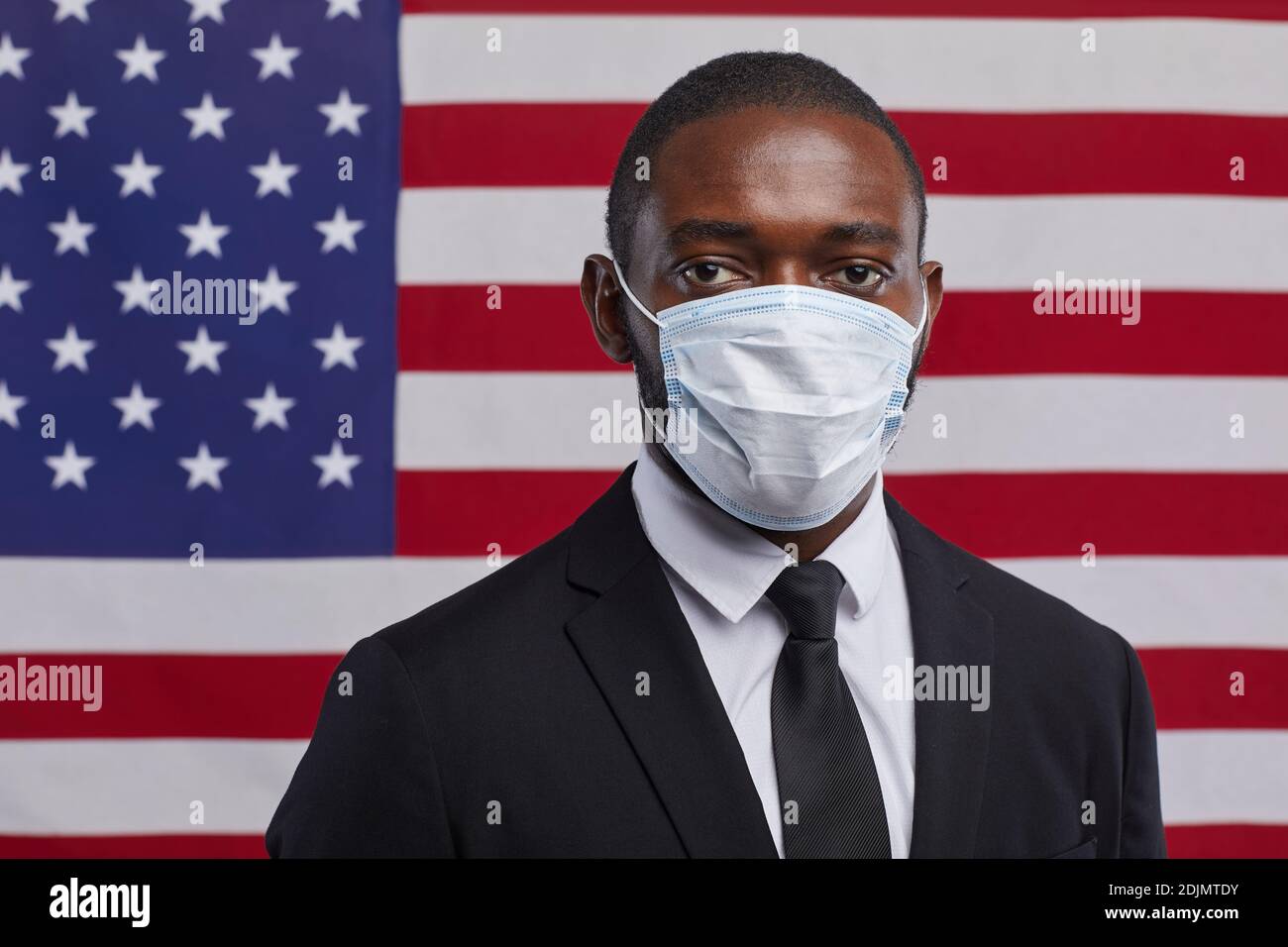 Portrait of African-American politician wearing mask and looking at camera while standing against USA flag background, copy space Stock Photo