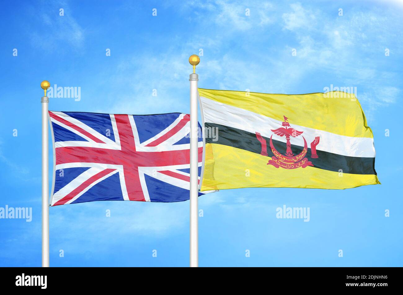 United Kingdom and Brunei two flags on flagpoles and blue cloudy sky Stock Photo