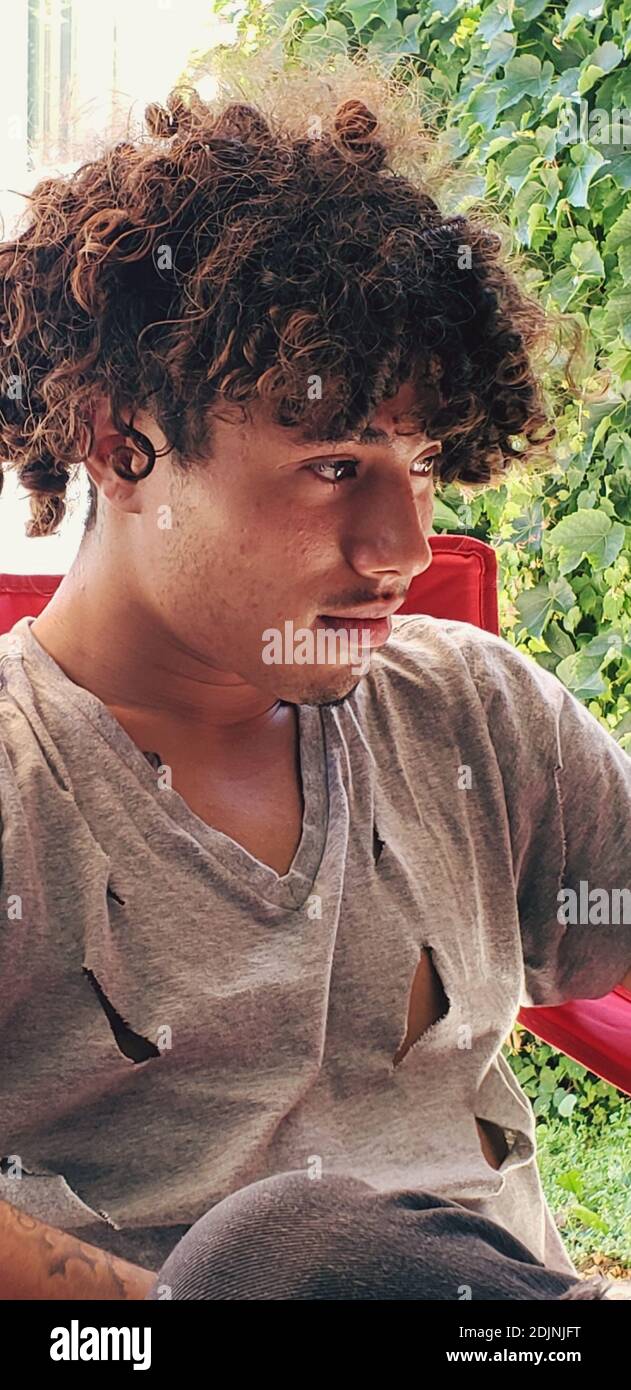 Teenage Boy With Curly Hair Looking Away While Sitting At Backyard Stock  Photo - Alamy