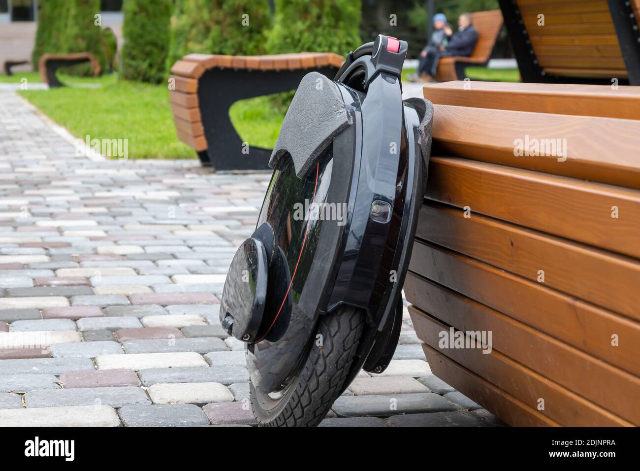 Black electric mono wheel, innovative personal vehicle, self-balancing electric unicycle, ecological urban transport of the future near a wooden bench Stock Photo