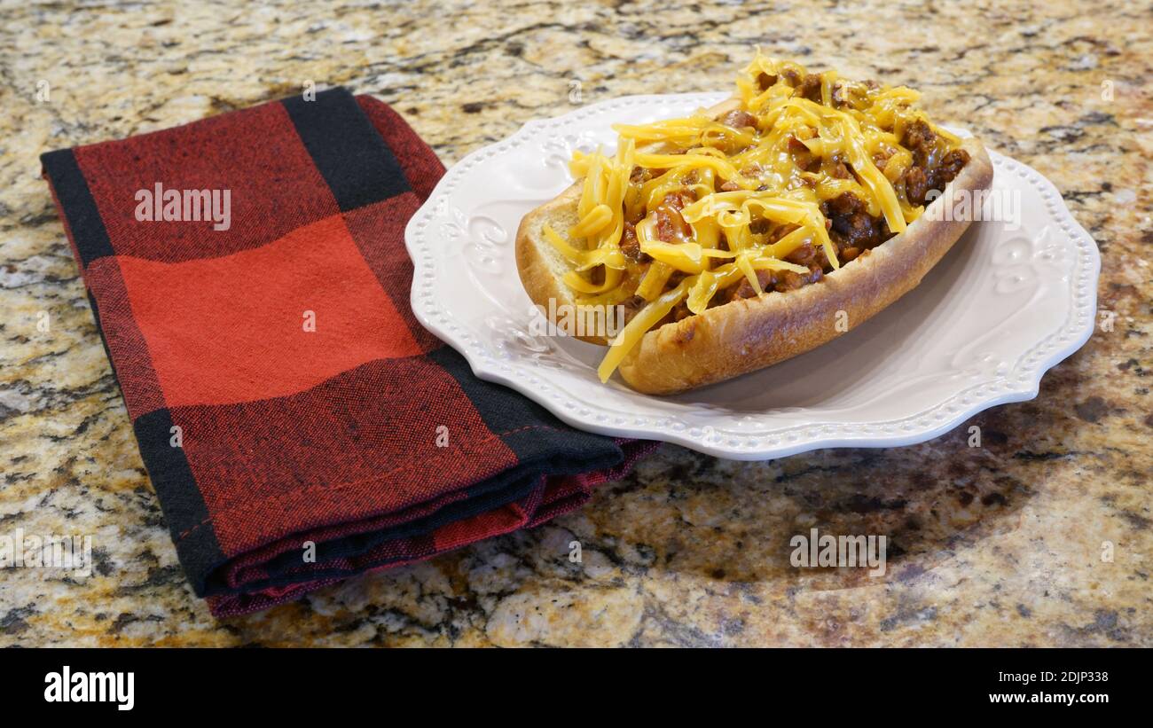 Homemade chili dog with cheddar cheese on a white plate. Stock Photo