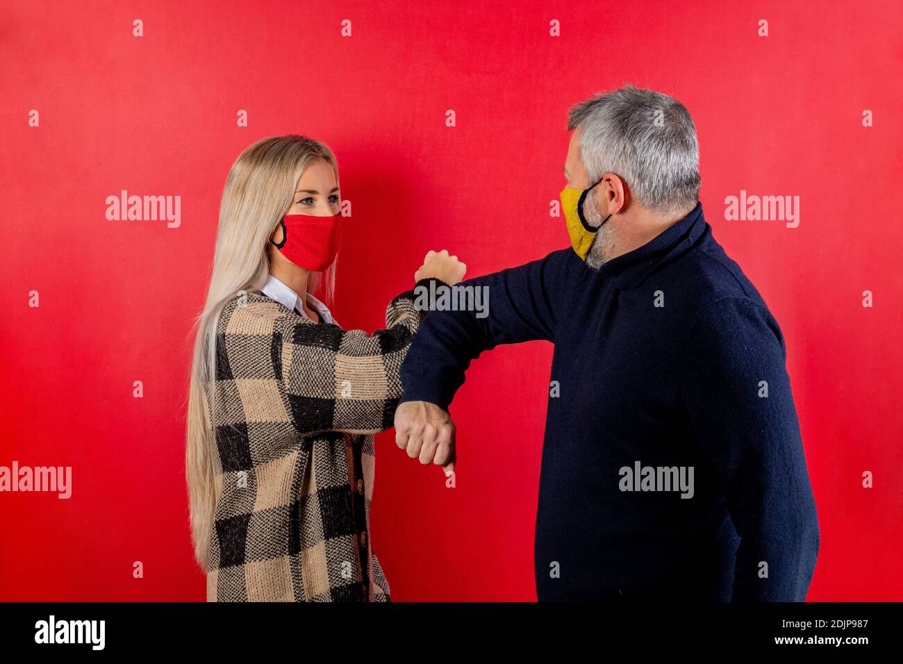 Girl and man greeting each other with the arms. Couple of people greetings with elbows on red background. People wearing face mask. Social distancing Stock Photo