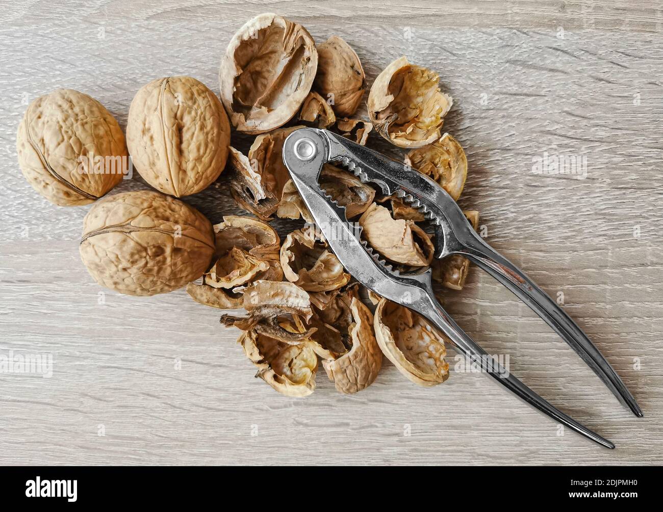 Three whole walnuts, nutshell and nutcracker on a wooden table Stock Photo