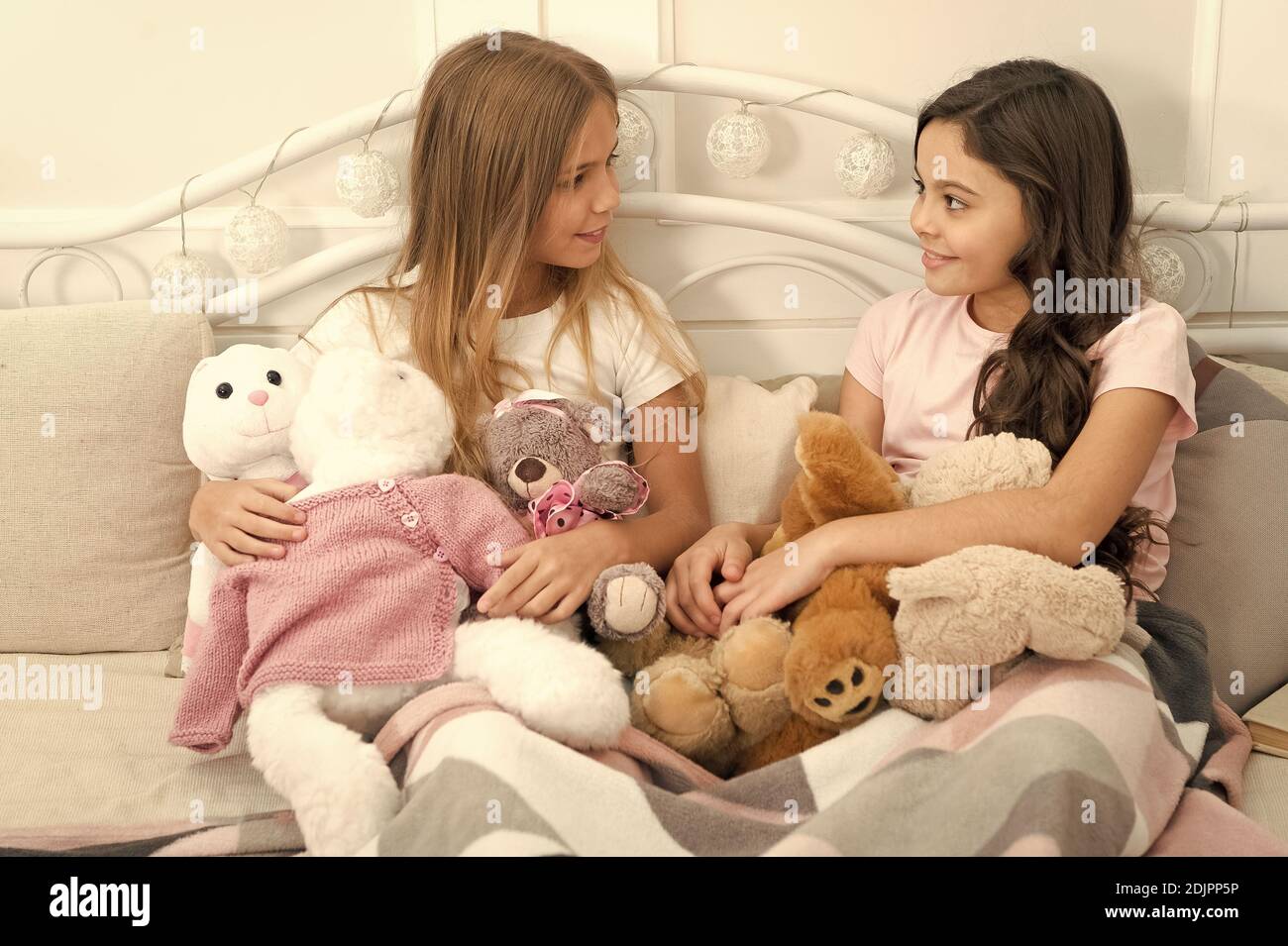 Sisters unite. Little sisters play toys in bed. Small sisters relax before nap time. Adorable sisters or friends in bedroom. Sisterhood and family. Friendship. Future is female. Stock Photo