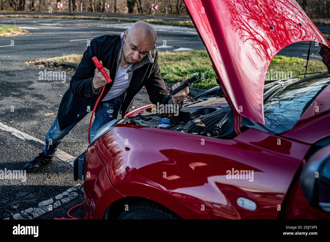A resigned, powerless driver tries to start a broken car using jumper