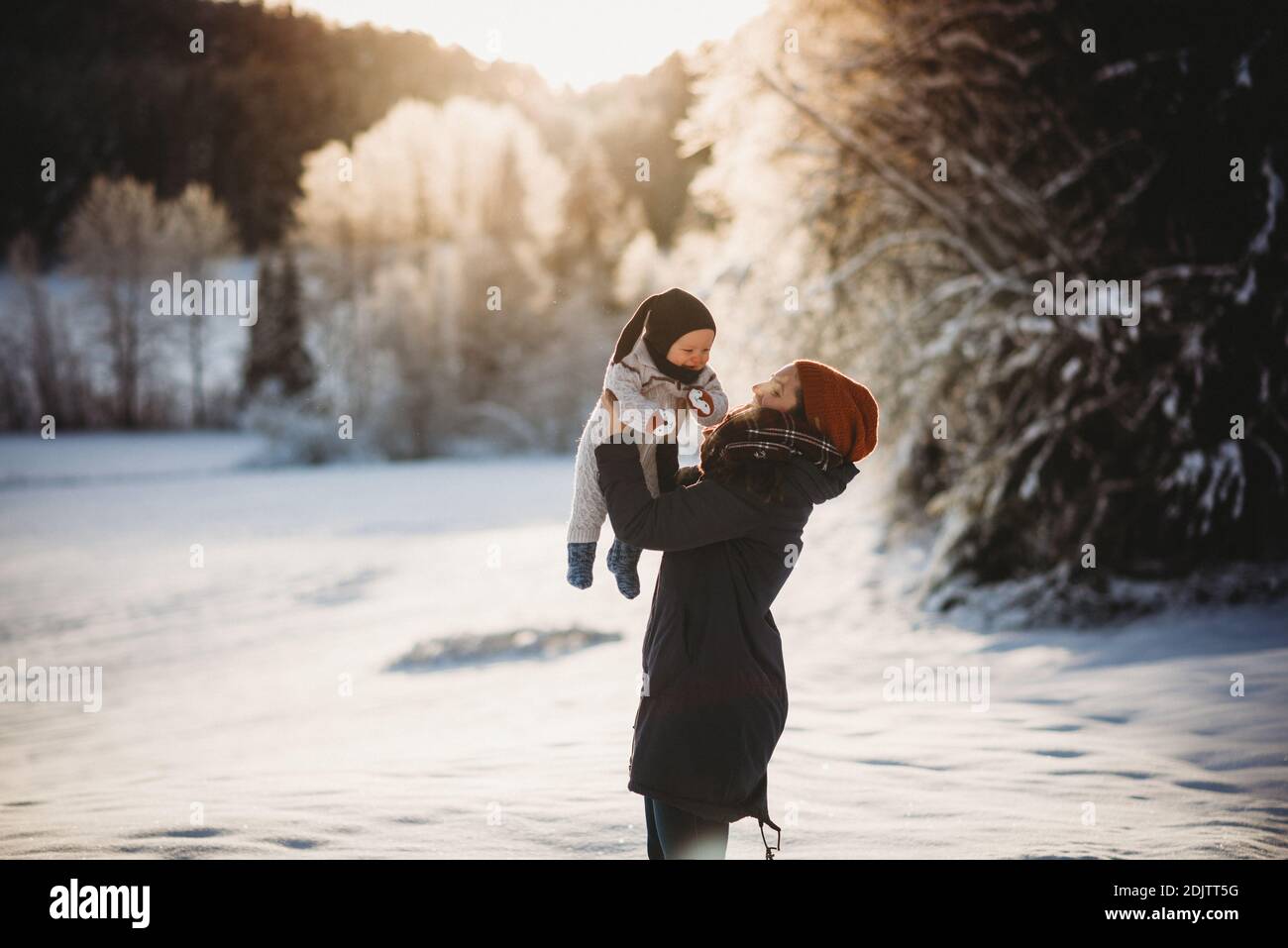 Mom holding baby up in snowy woods during sunset in Norway in winter Stock Photo