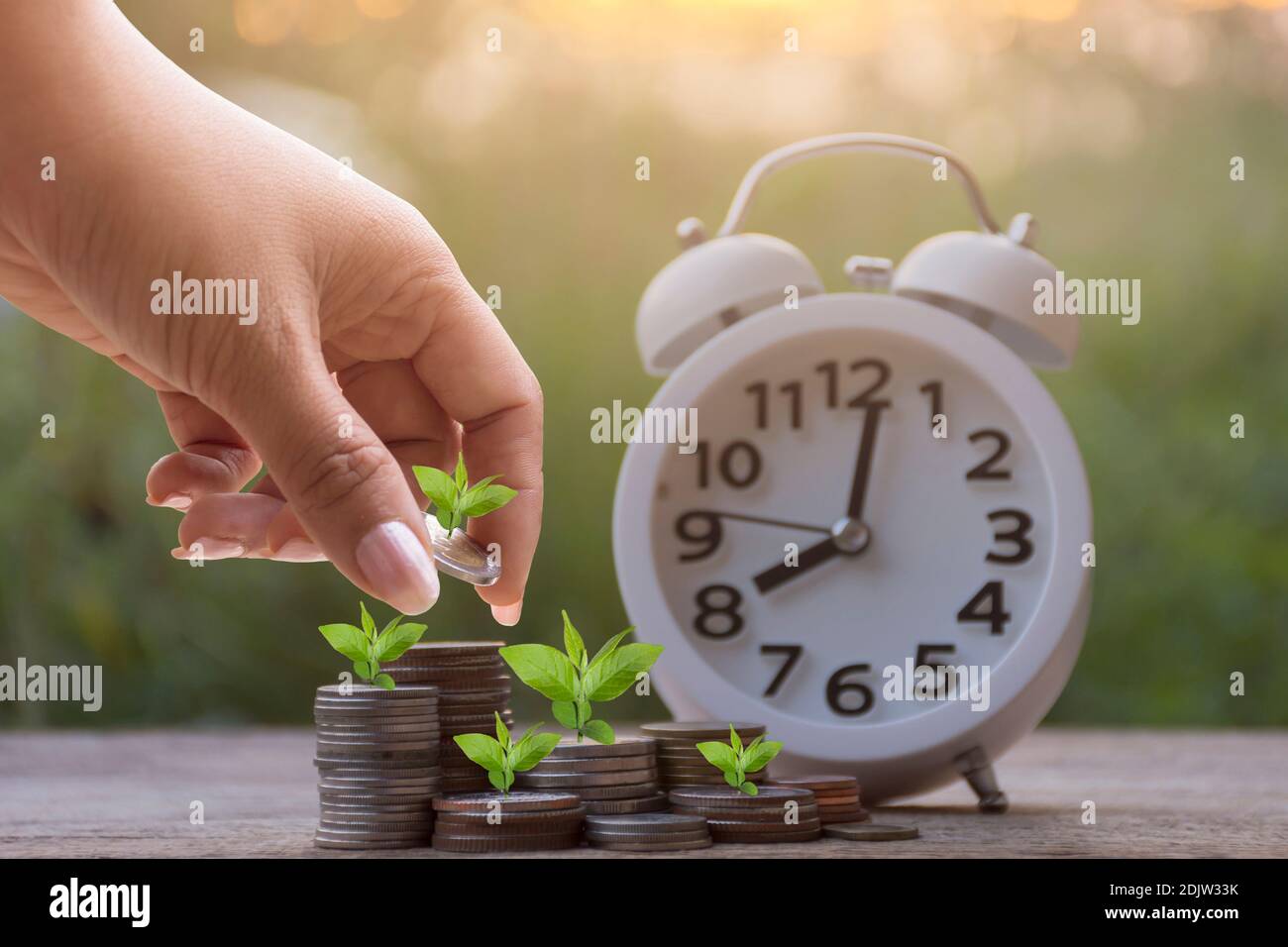 Cropped Hand Of Woman Stacking Coins By Alarm Clock Stock Photo