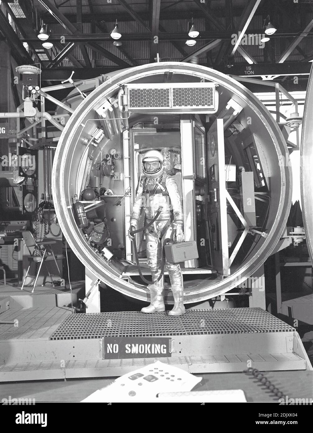 Astronaut John H. Glenn Jr., suited with hose to suit ventilation unit  attached, during altitude chamber test in 1961. He is standing in the  entrance to the test chamber with his helmet