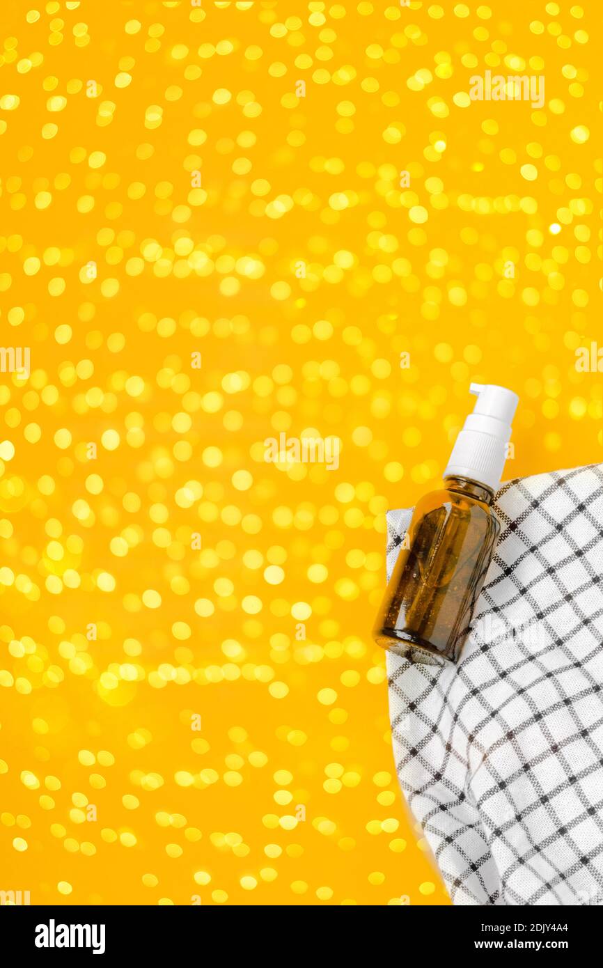 Festive lubricant or antibacterial gel in pump bottle container on a checkered blanket and yellow backdrop. Illuminating glitter as 2021 year symbol Stock Photo