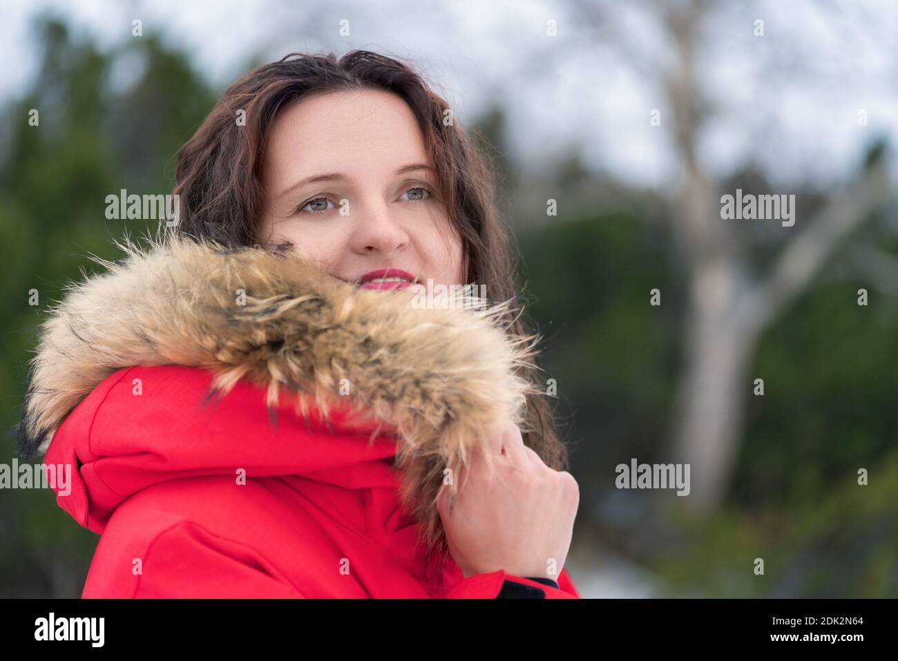 Young woman hides her face from cold in hood of red winter jacket ...