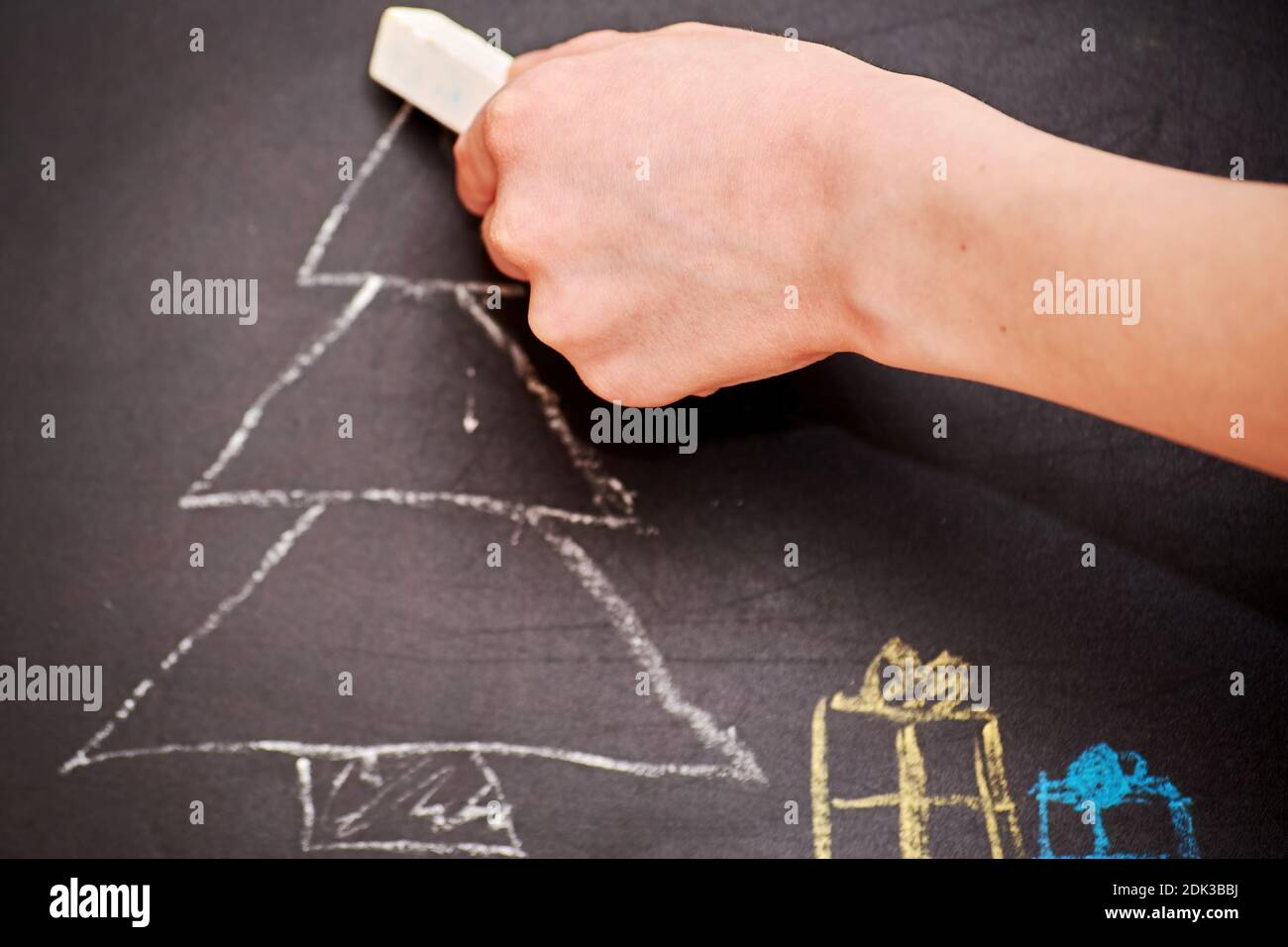 Children hand drawing a Christmas tree and presents on the chalkboard. Kids leisure activity and hobby Stock Photo