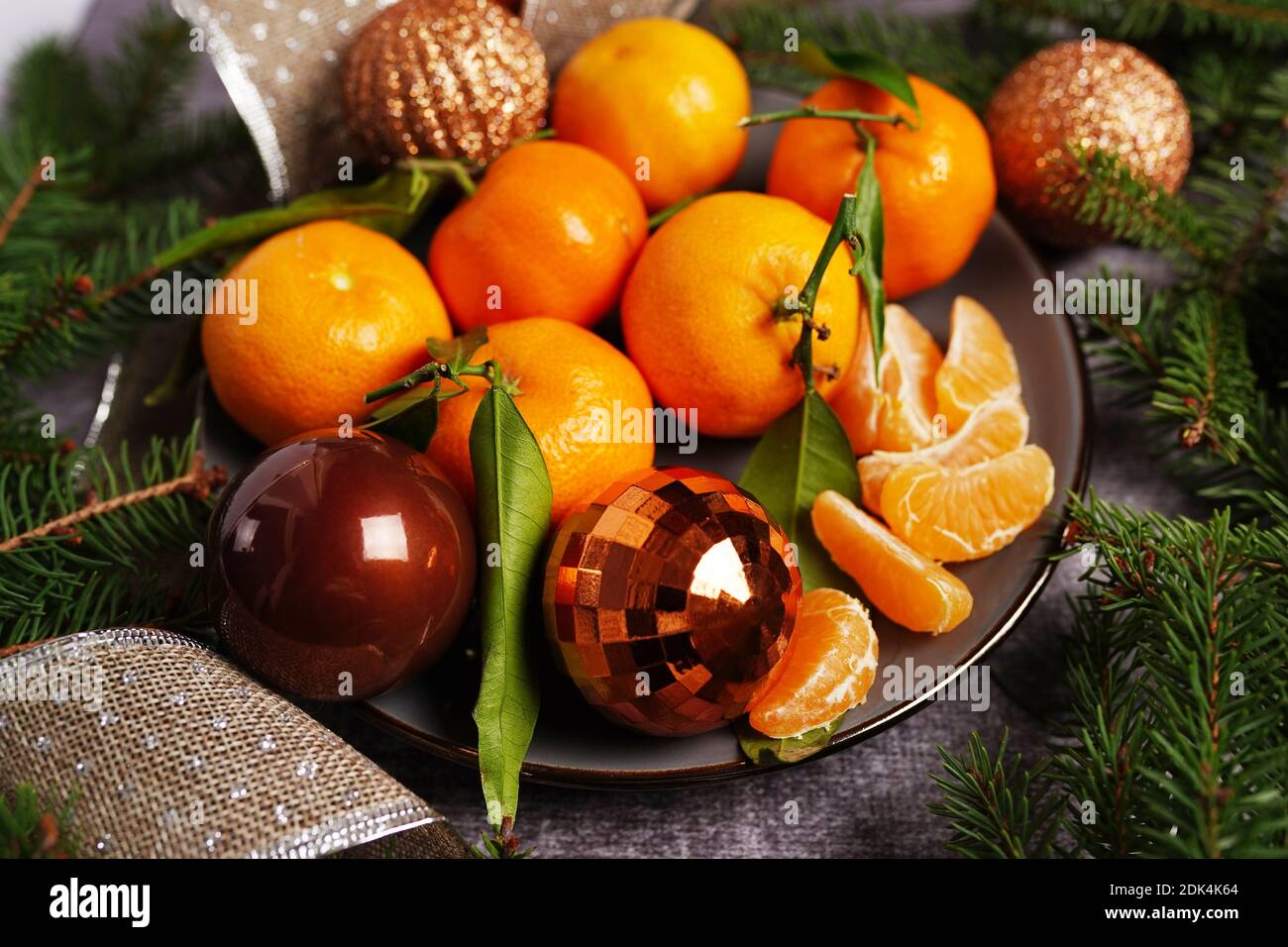 Fresh Clementines or Tangerines on plste on gray Table with christmas balls and Tree Branches Stock Photo