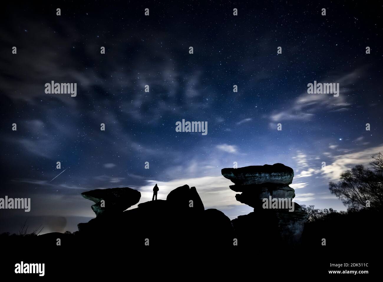A man watches a meteor during the Geminid meteor shower over Brimham Rocks, a collection of balancing rock formations in the Nidderdale Area of Outstanding Natural Beauty in North Yorkshire. Stock Photo