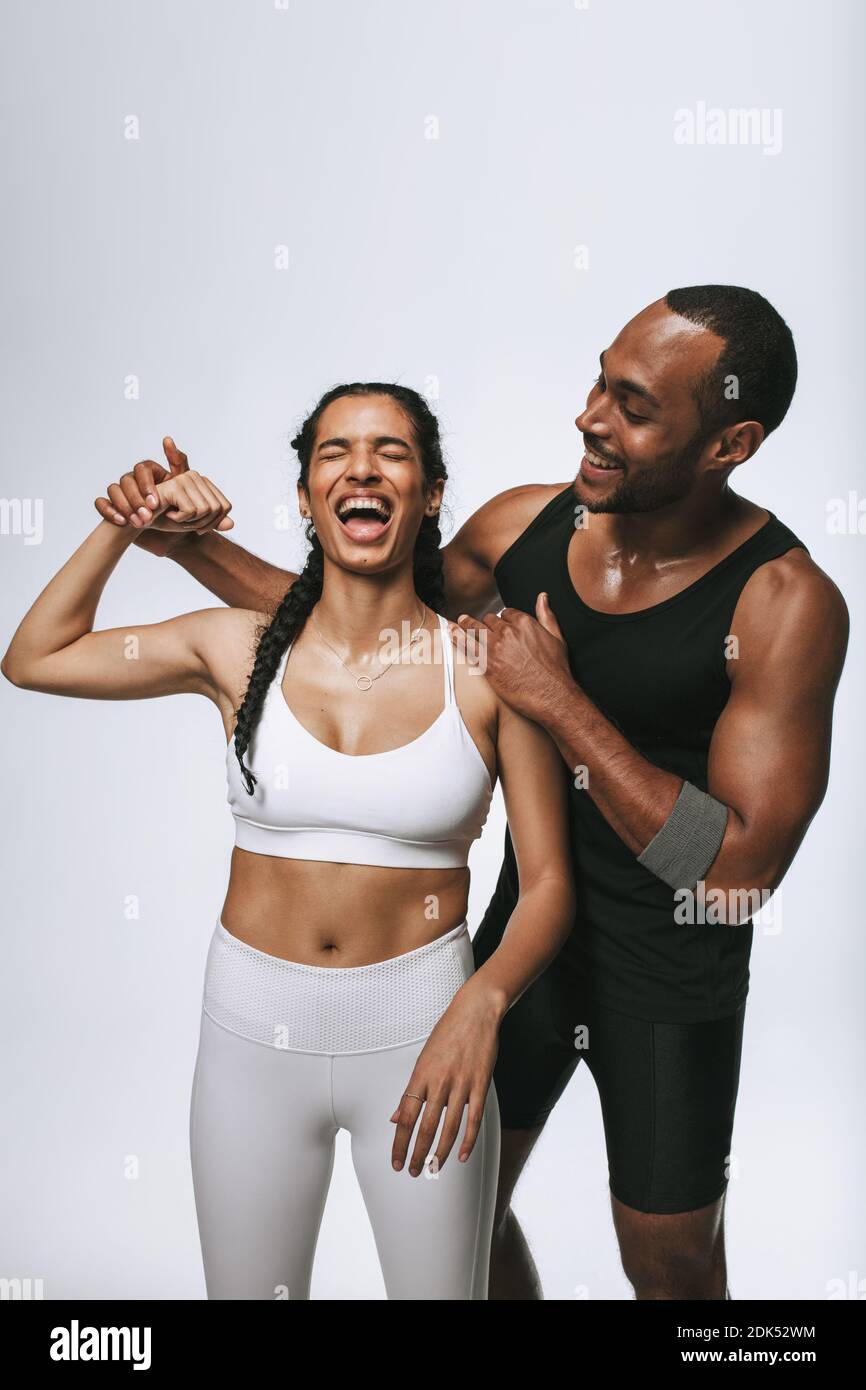 Friends having fun at the gym. Happy woman in fitness wear showing her biceps with her male friend by her side. Stock Photo