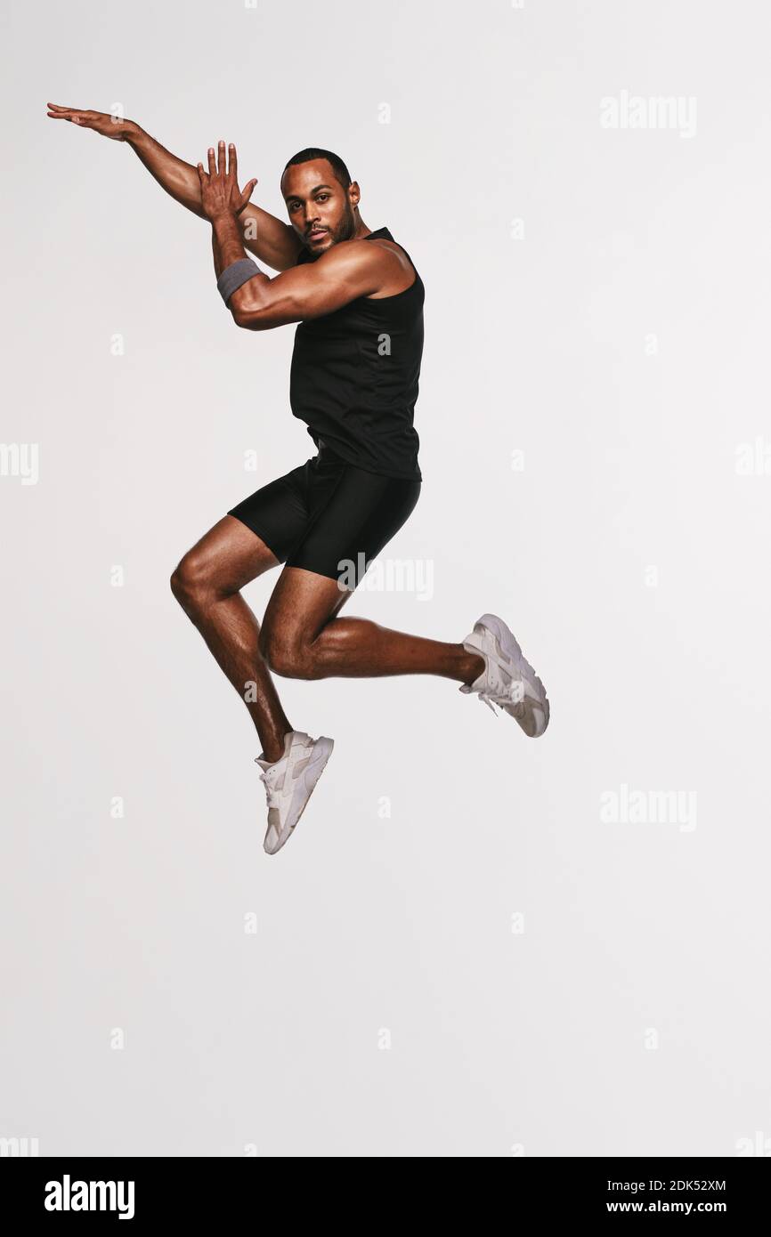 Portrait of african american athlete jumping in air. Fit man doing exercise on white background. Stock Photo