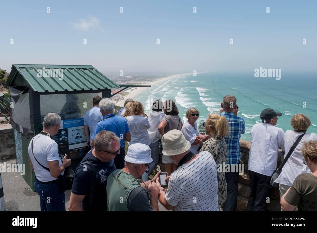 Tourists look over False Bay from the Shark Spotters shelter on Boyes Drive overlooking Muizenberg Beach, False Bay, Cape Town, South Africa. Stock Photo