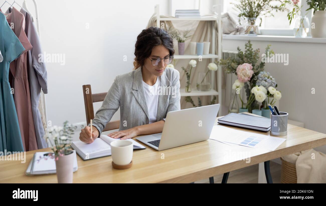 Busy female designer sitting by pc making notes in planner Stock Photo