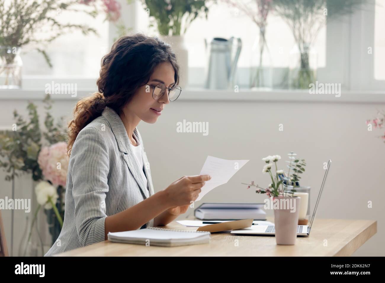 Focused young businesswoman reading paper letter at work desk Stock Photo