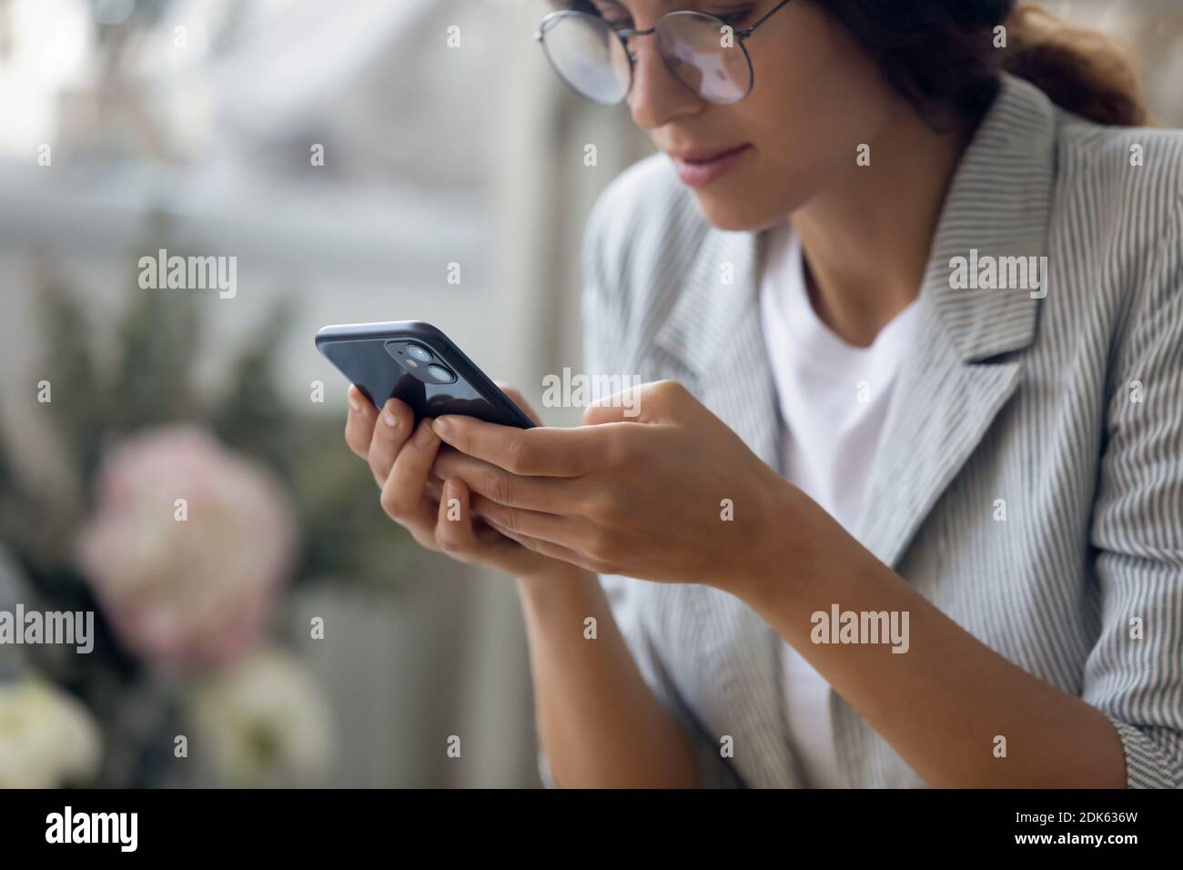 Concentrated millennial female in glasses holding smartphone making answering call Stock Photo