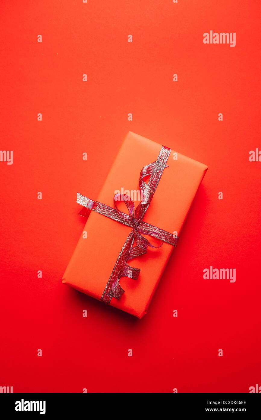 Gift box wrapped in red paper with gold ribbon bow on a red background ...