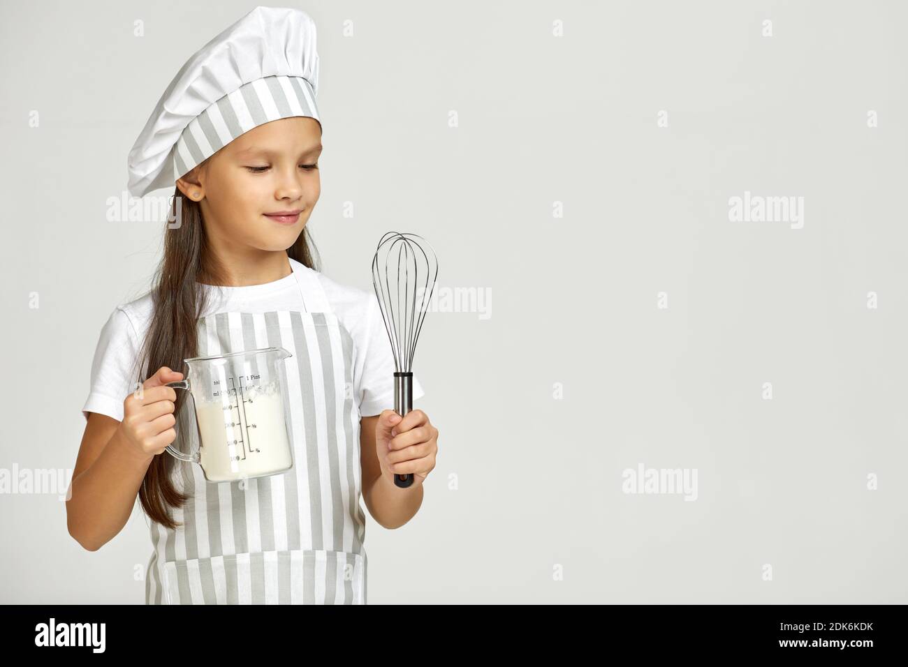 little girl in chef hat and apron with flour in measuring cup and whisk