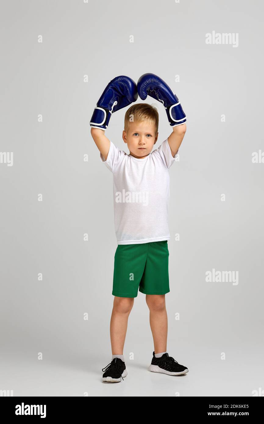 little boxing fighter boy in blue boxer gloves is gesturing victory