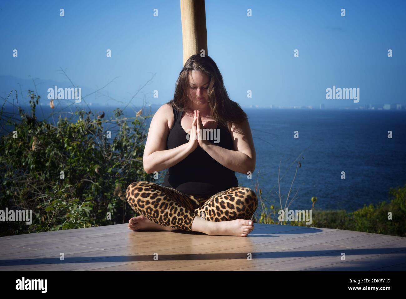 Woman Meditating While Sitting On Wooden Floor Against Sea And Sky Stock Photo