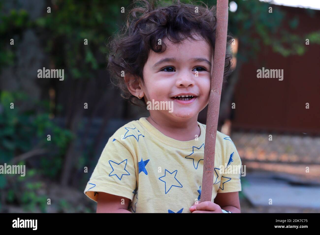 An Indian little child is playing with a wooden stick and laughing Stock Photo