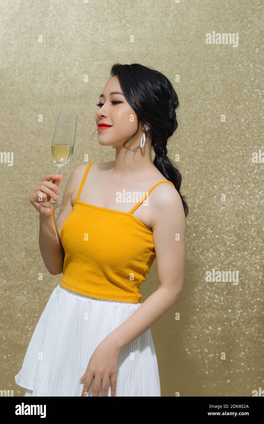 party, drinks, holidays, luxury and celebration concept - smiling woman in evening dress with glass of sparkling wine over gold background. Stock Photo