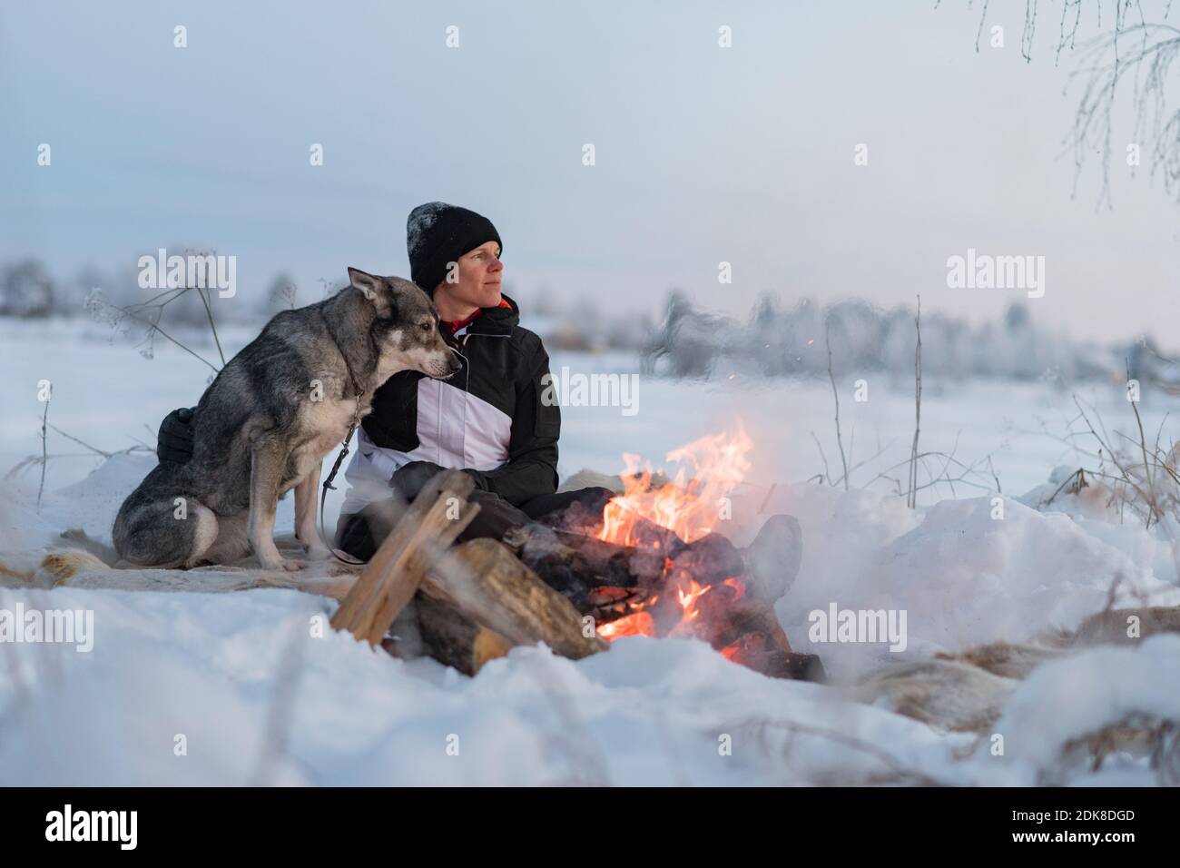 Woman with dog sitting at camp fire Stock Photo