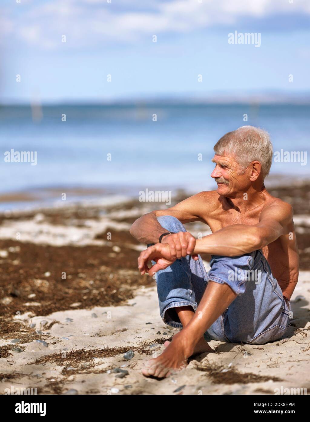 Elderly man in jeans sitting on sandy beach Stock Photo Alamy
