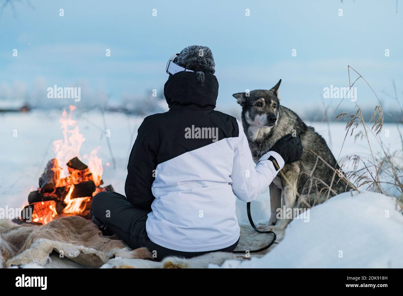 Woman with dog sitting at camp fire Stock Photo