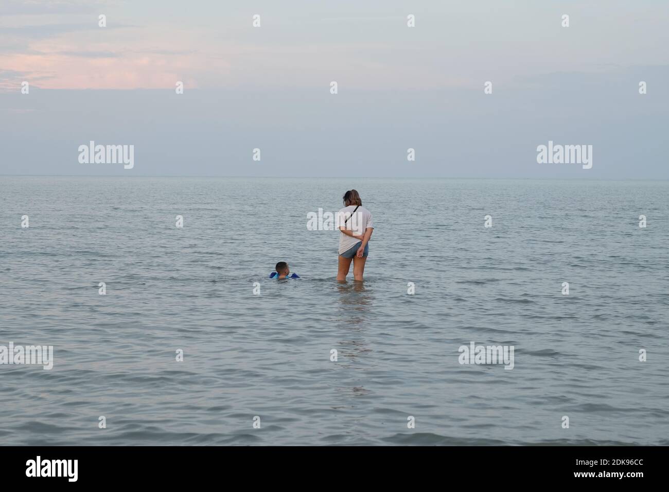 Rear View Of Mother With Son In Sea Against Sky Stock Photo