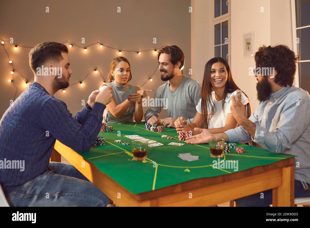 Group of excited friends with playing cards in hands sitting, betting and playing poker Stock Photo