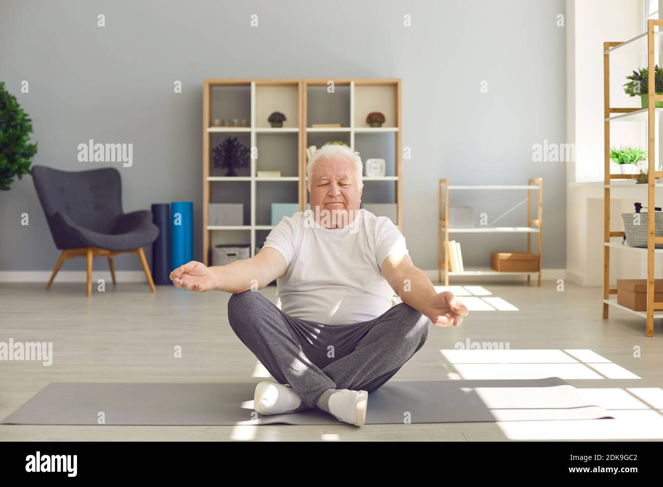 Senior man sitting in lotus position on fitness mat and meditating with eyes closed Stock Photo