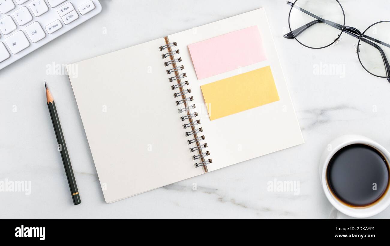 Top view of office table desk cozy work concept with keyboard, notebook, pencil, eyeglasses and coffee on bright marble white background. Stock Photo