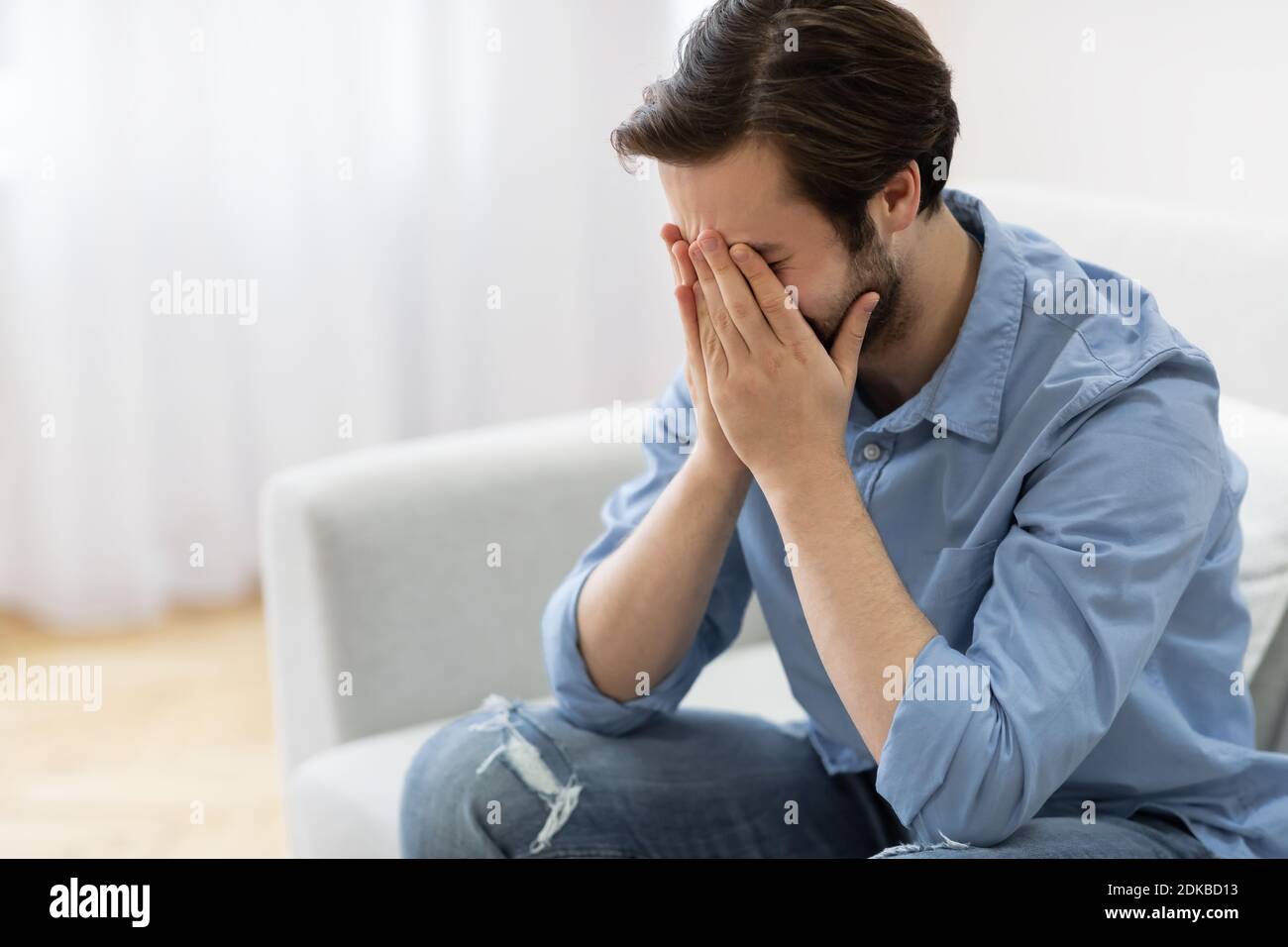 Frustrated Man Crying Covering Face Sitting On Sofa At Home Stock Photo