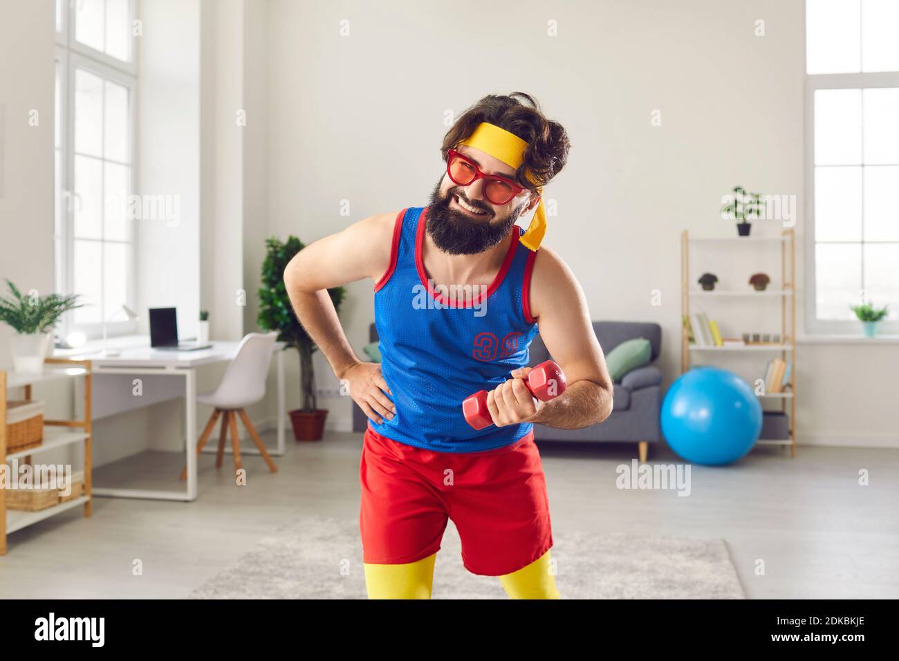 Funny and hardy man in colorful colored sportswear doing sports workout with dumbbells at home. Stock Photo