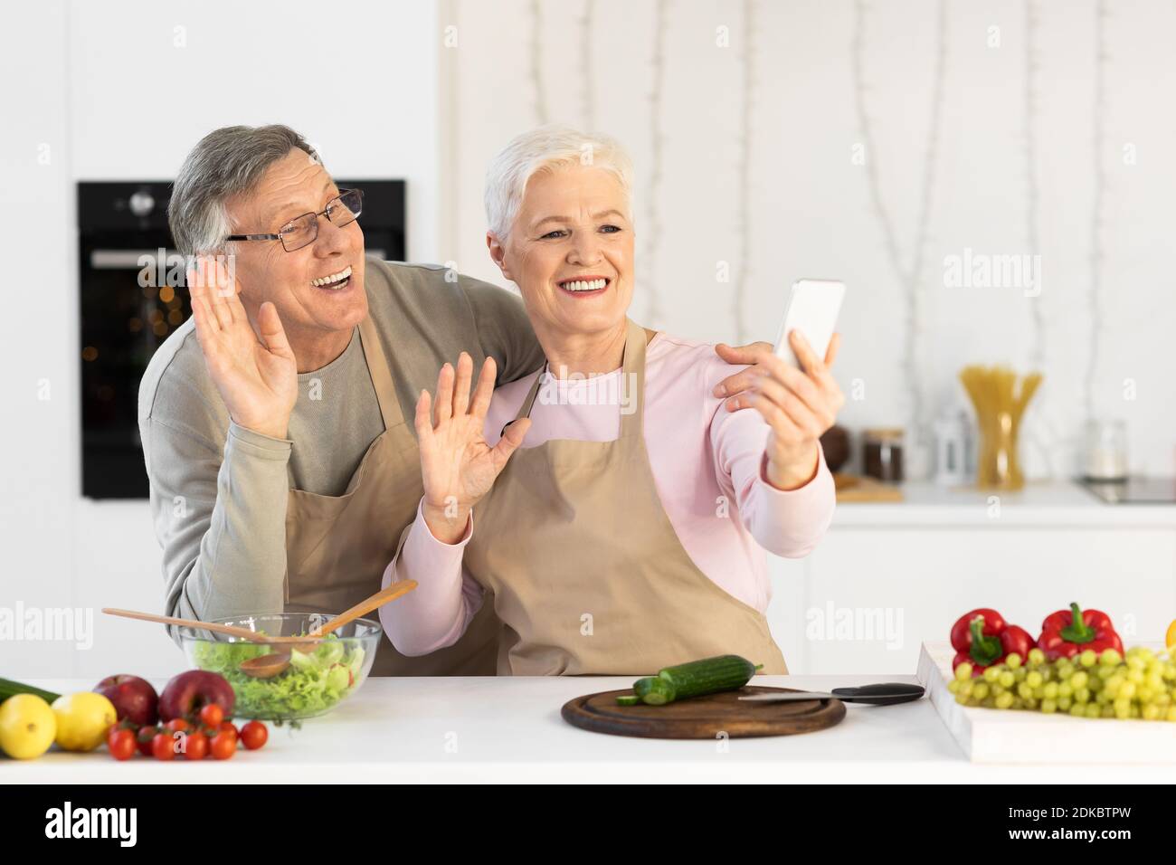 Senior Couple Making Video Call Using Mobile Phone In Kitchen Stock Photo