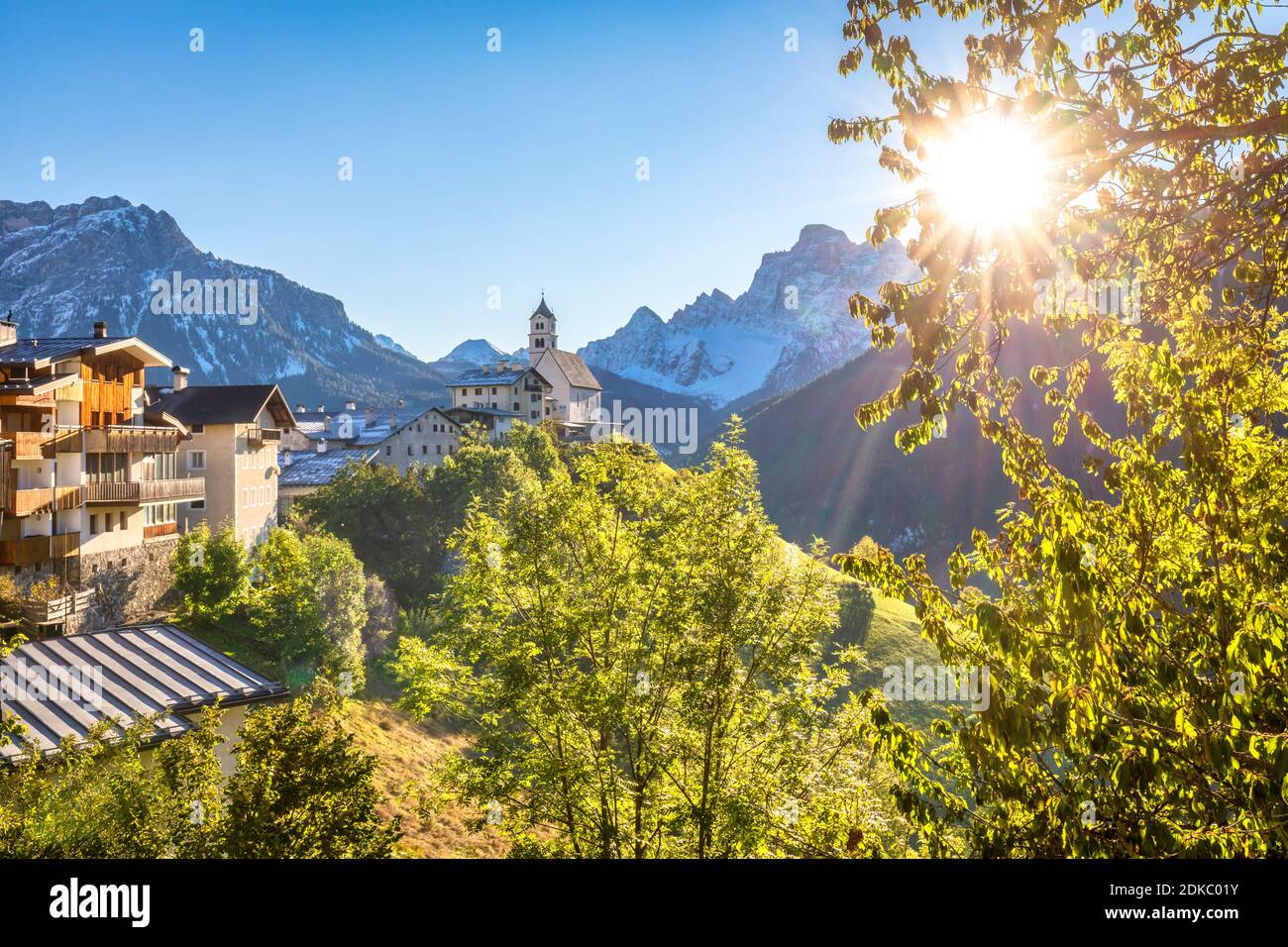 a classic glimpse of the village of Colle Santa Lucia dominated by the parish church and Mount Pelmo in the background, autumn scene with the sun in the sky, Agordino, province of Belluno, Veneto, Italy, Europe Stock Photo