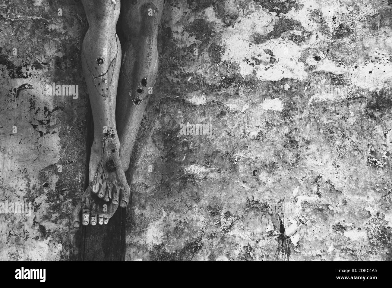 Religious background. Passion, suffer concept. Closeup of old wooden crucifix with peeling paint against grungy stone wall in church.  Black white Stock Photo