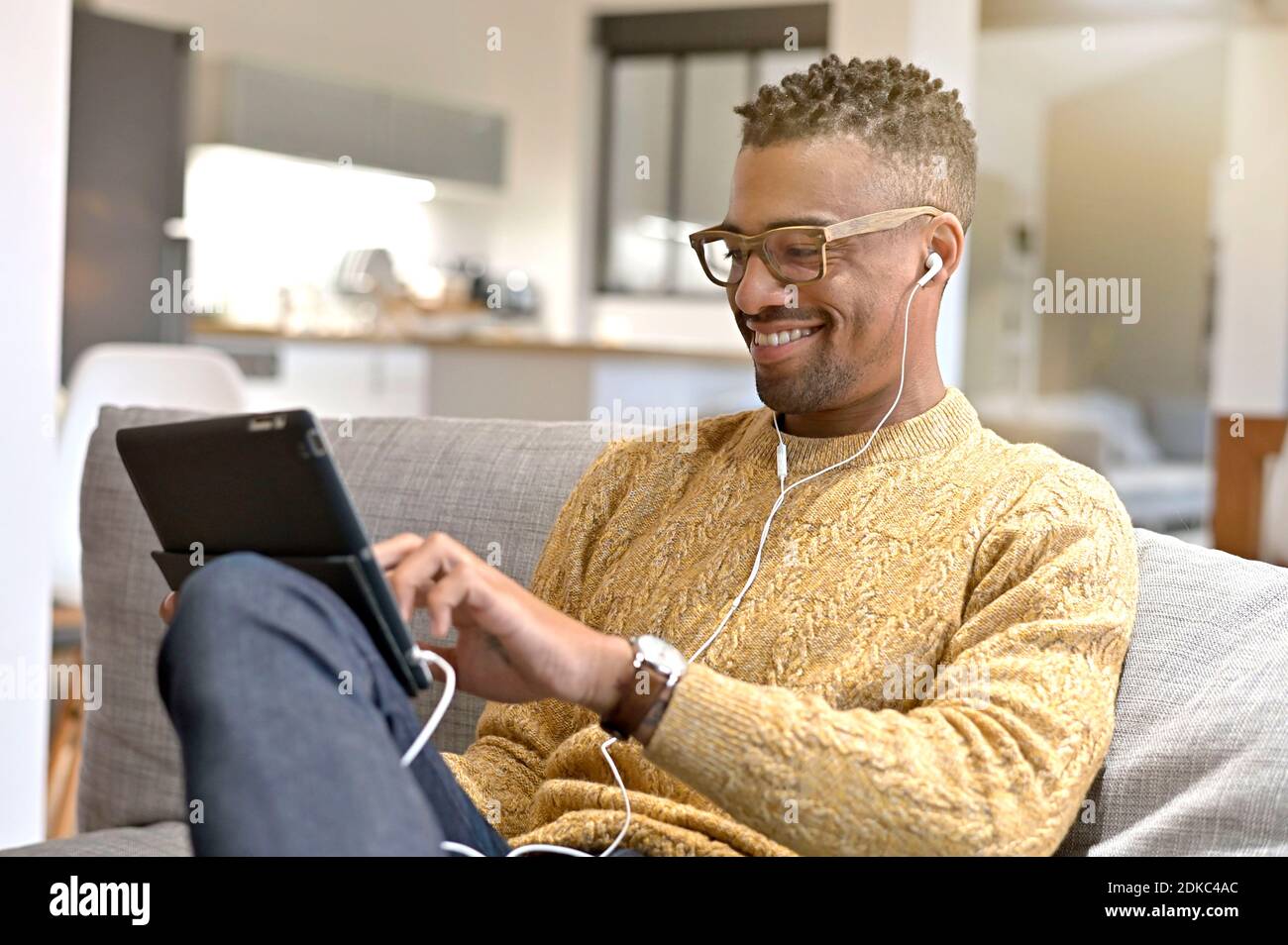 Young trendy afro-amercian guy relaxing in sofa watching movie on digital tablet Stock Photo